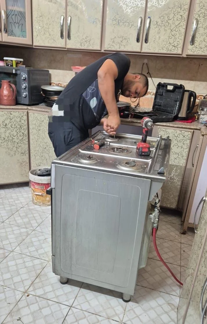 فني تصليح افران يفحص موقد الغاز داخل المطبخ لضمان عمل الشعلات بكفاءة